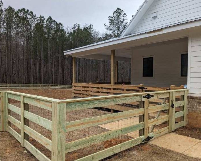 Ranch rail fence corner with house in background.