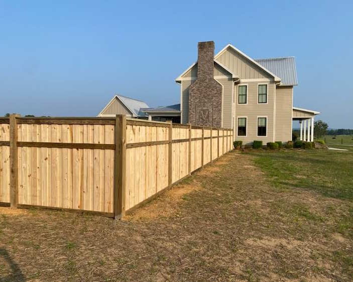 Wood privacy fence corner with house in background.